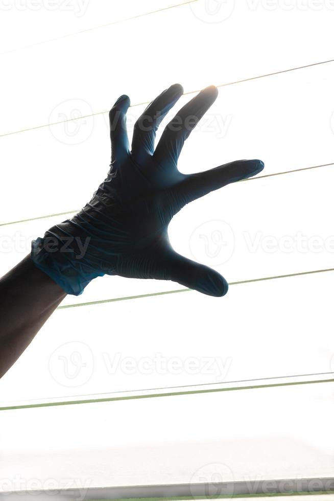 mão de silhueta usando luvas azuis com persianas de luz. foto