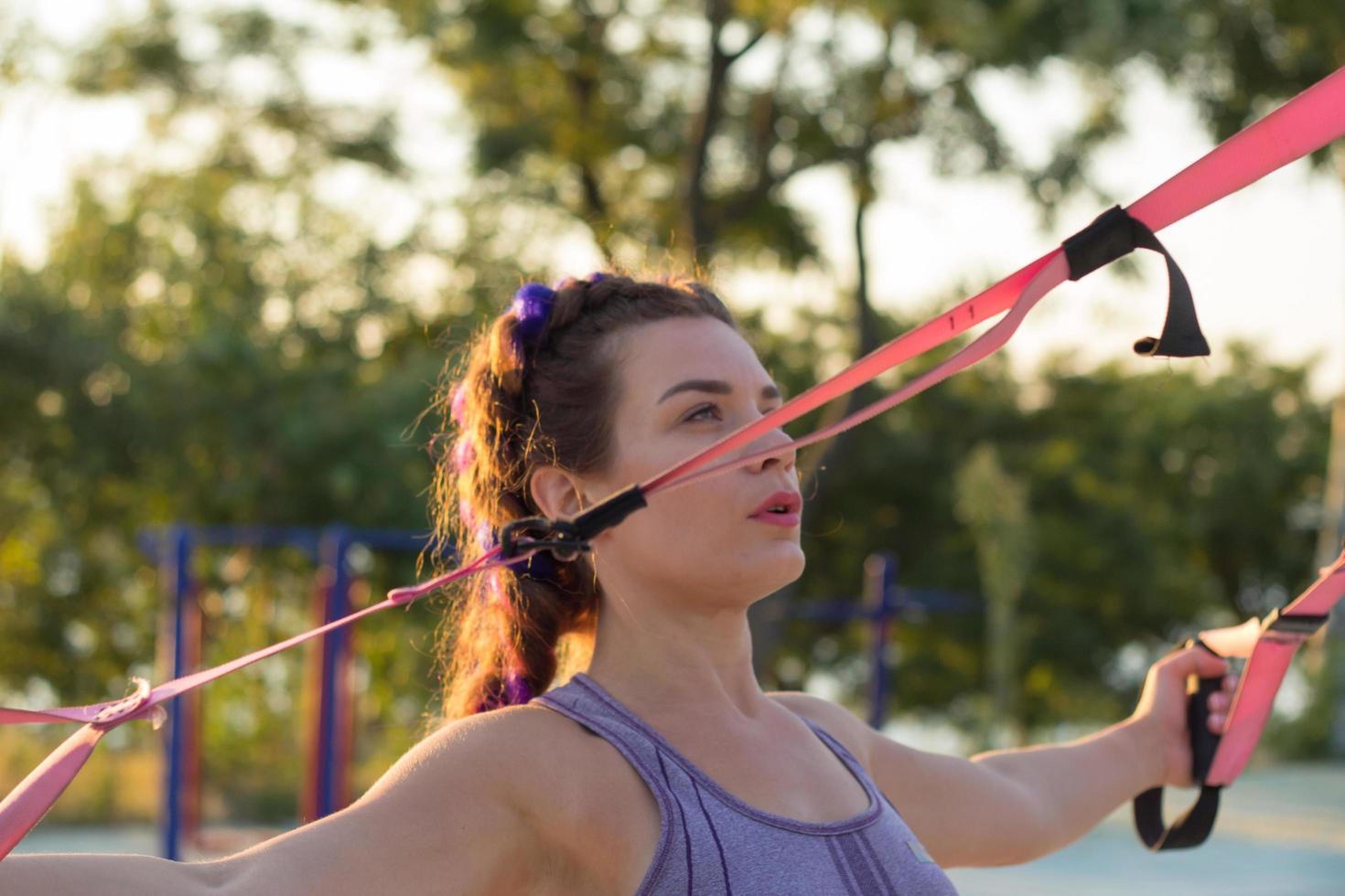 bela mulher apta no treinamento esportivo rosa e roxo na academia ao ar livre de manhã, exercícios com tiras de suspensão no parque foto