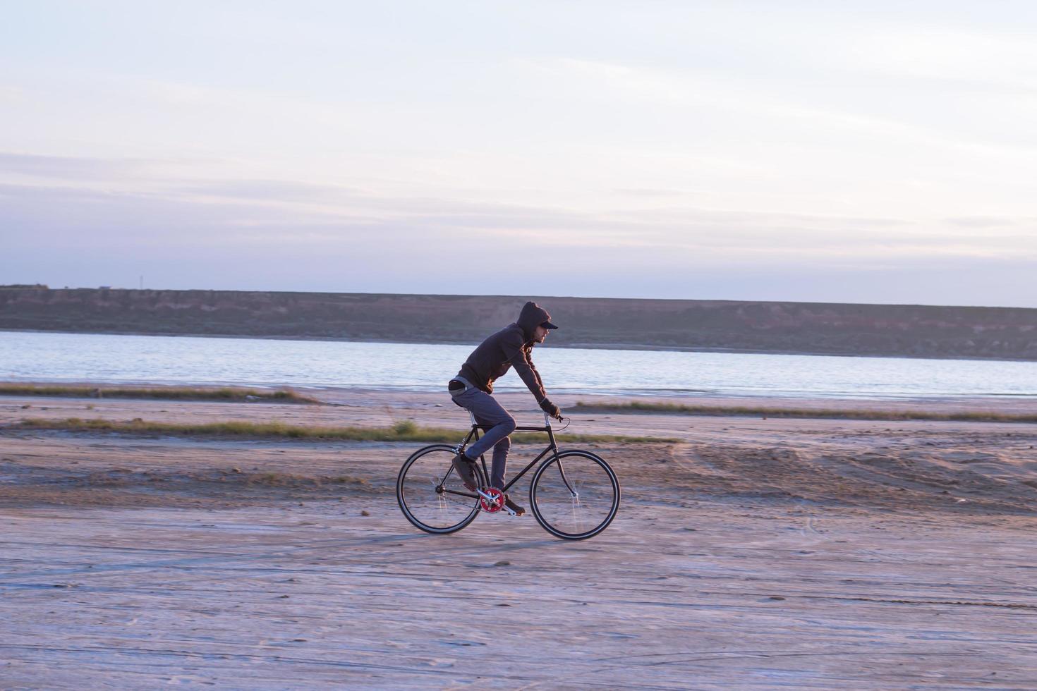 cavaleiro sozinho na bicicleta de estrada de engrenagem fixa andando no deserto perto do rio, fotos de ciclista de turista hipster.