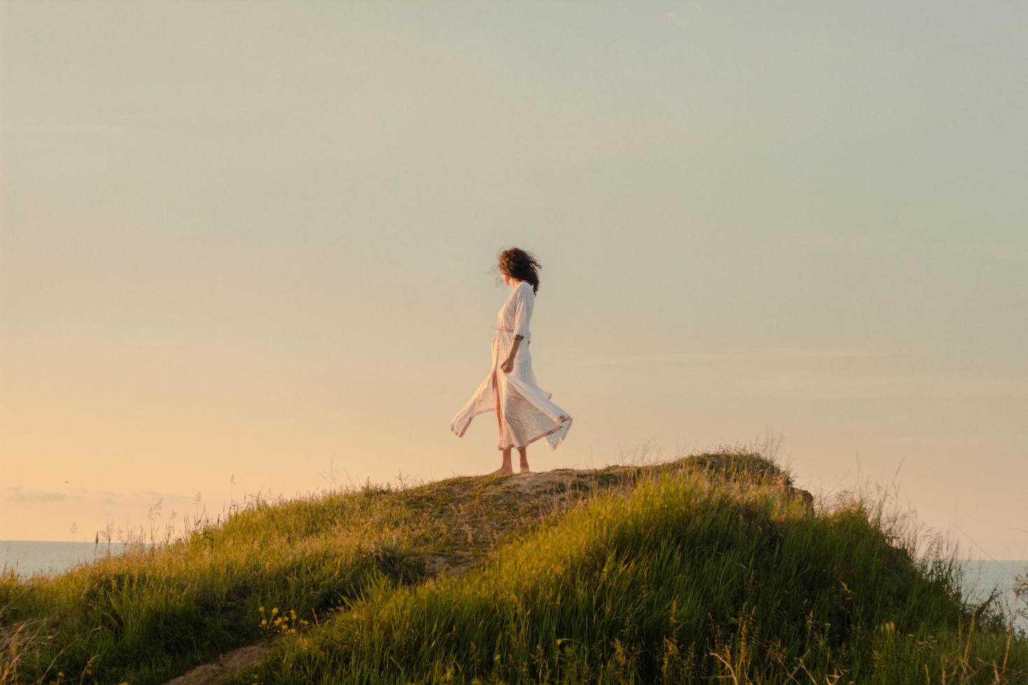 jovem caminhando na praia de manhã em lindo vestido branco. apto feminino se divertindo durante o nascer do sol. foto