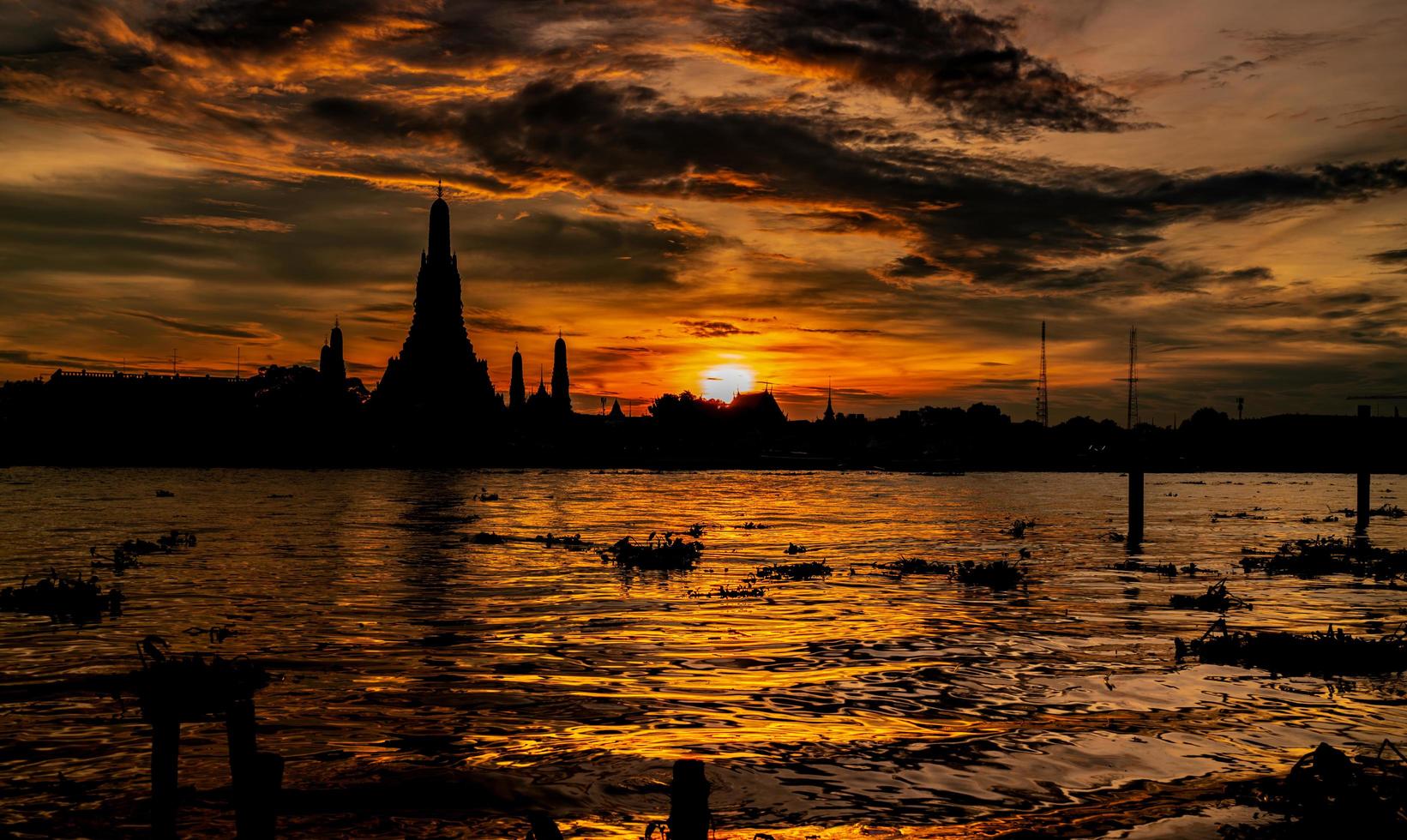 rio e wat arun ratchawararam ao pôr do sol com lindo céu laranja e nuvens. o templo budista wat arun é o marco em bangkok, tailândia. silhueta dramática céu e templo na tailândia. foto