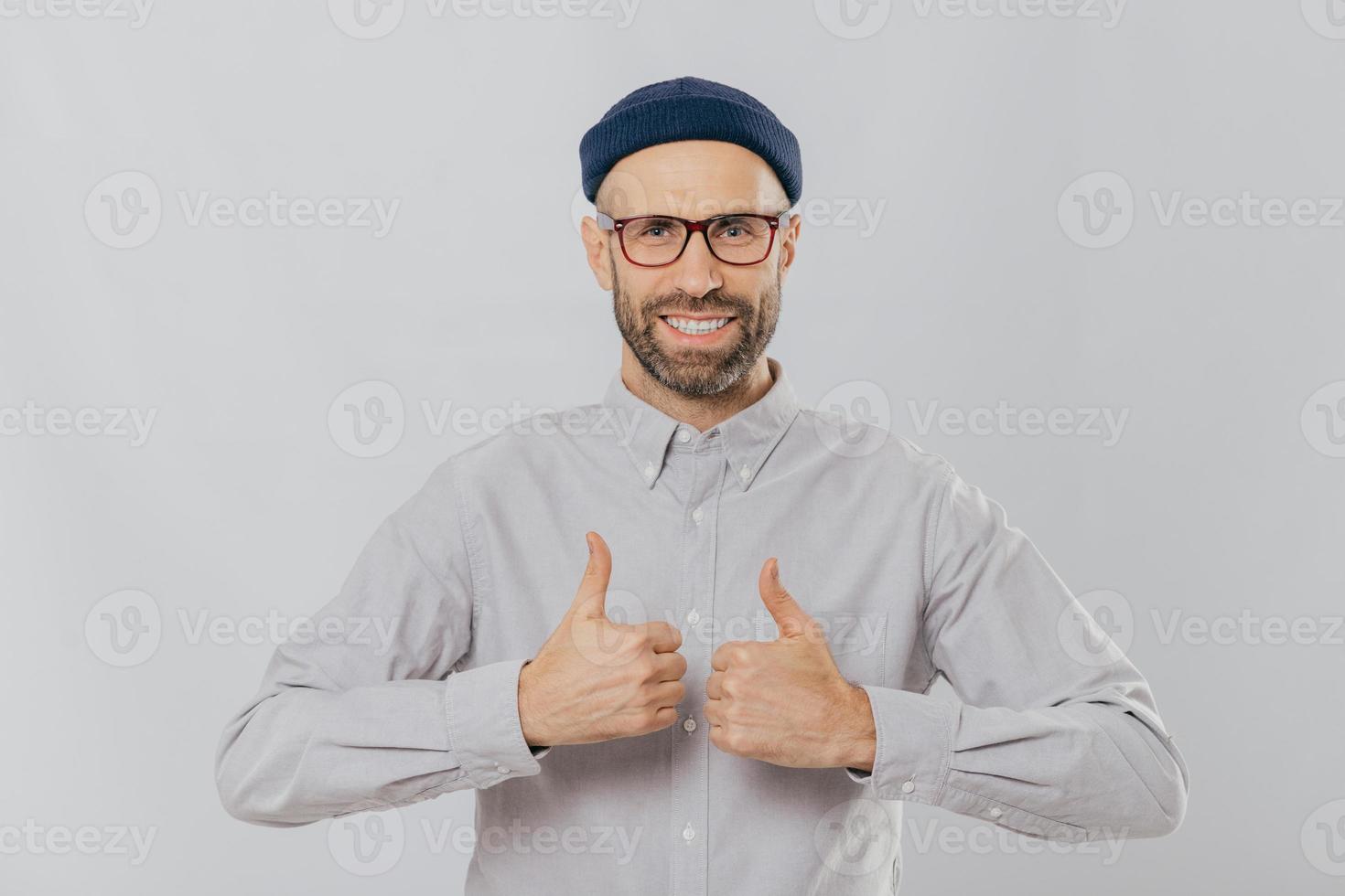 feliz homem não barbeado levanta os polegares, sorri amplamente, satisfeito com a ótima escolha, tem barba escura, vestido com camisa formal, isolado sobre fundo branco, aprova a ideia legal foto