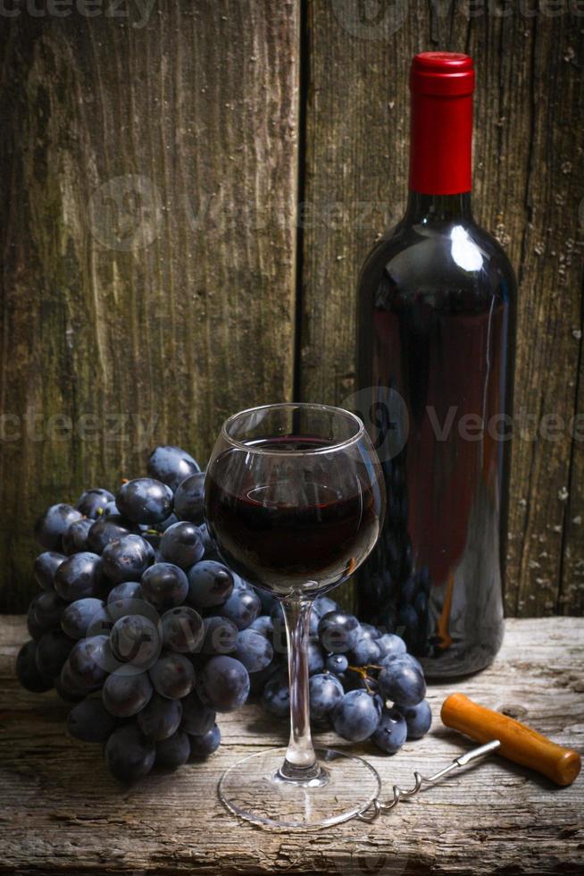 garrafa de vinho tinto, uva e saca-rolhas na mesa de madeira foto
