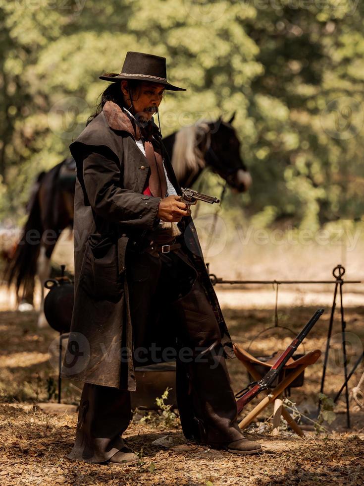 um vaqueiro sênior em pé com uma arma para proteger a segurança do acampamento na área oeste foto