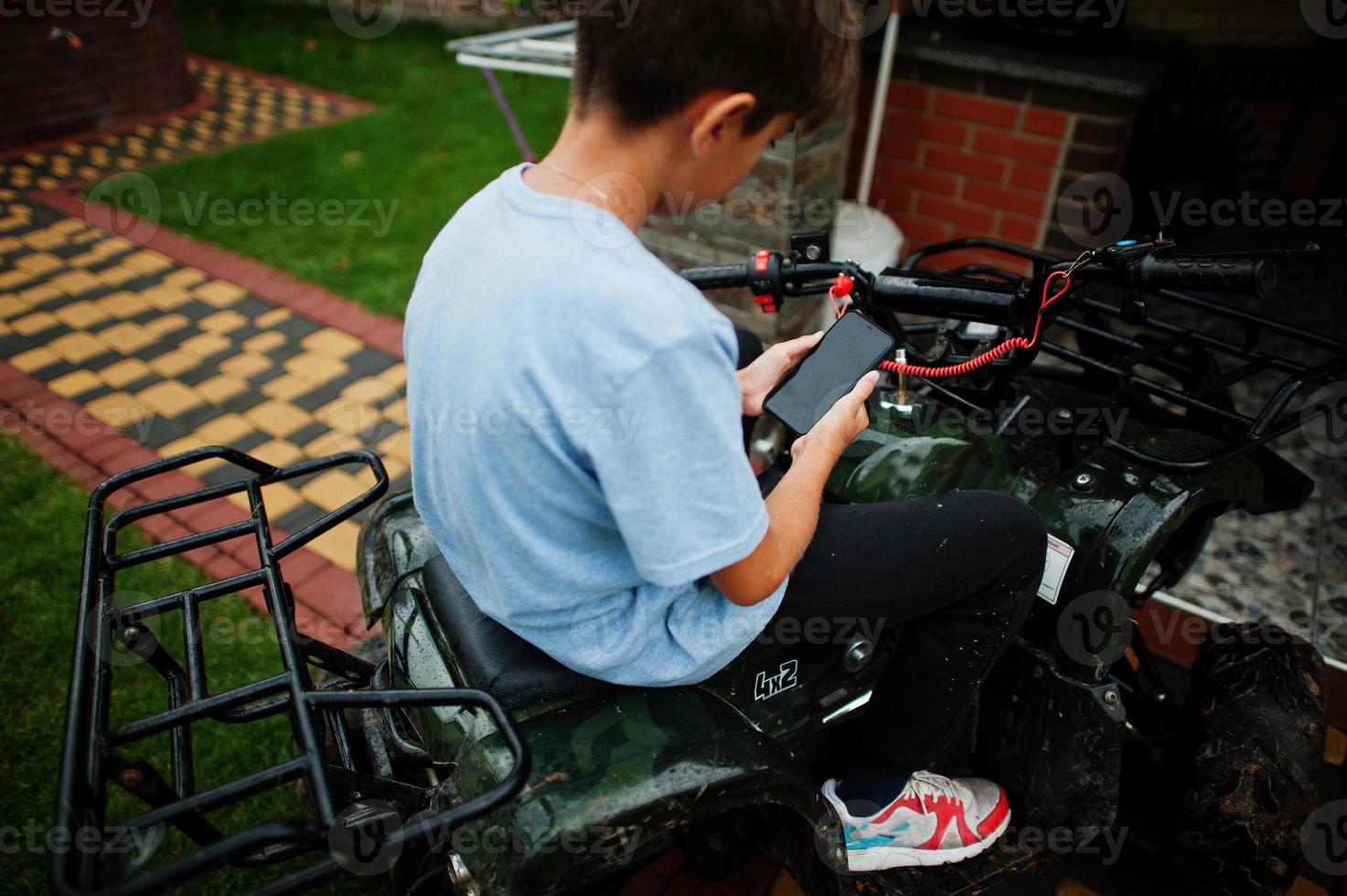 menino em quadriciclo de quatro rodas com telefone celular. foto