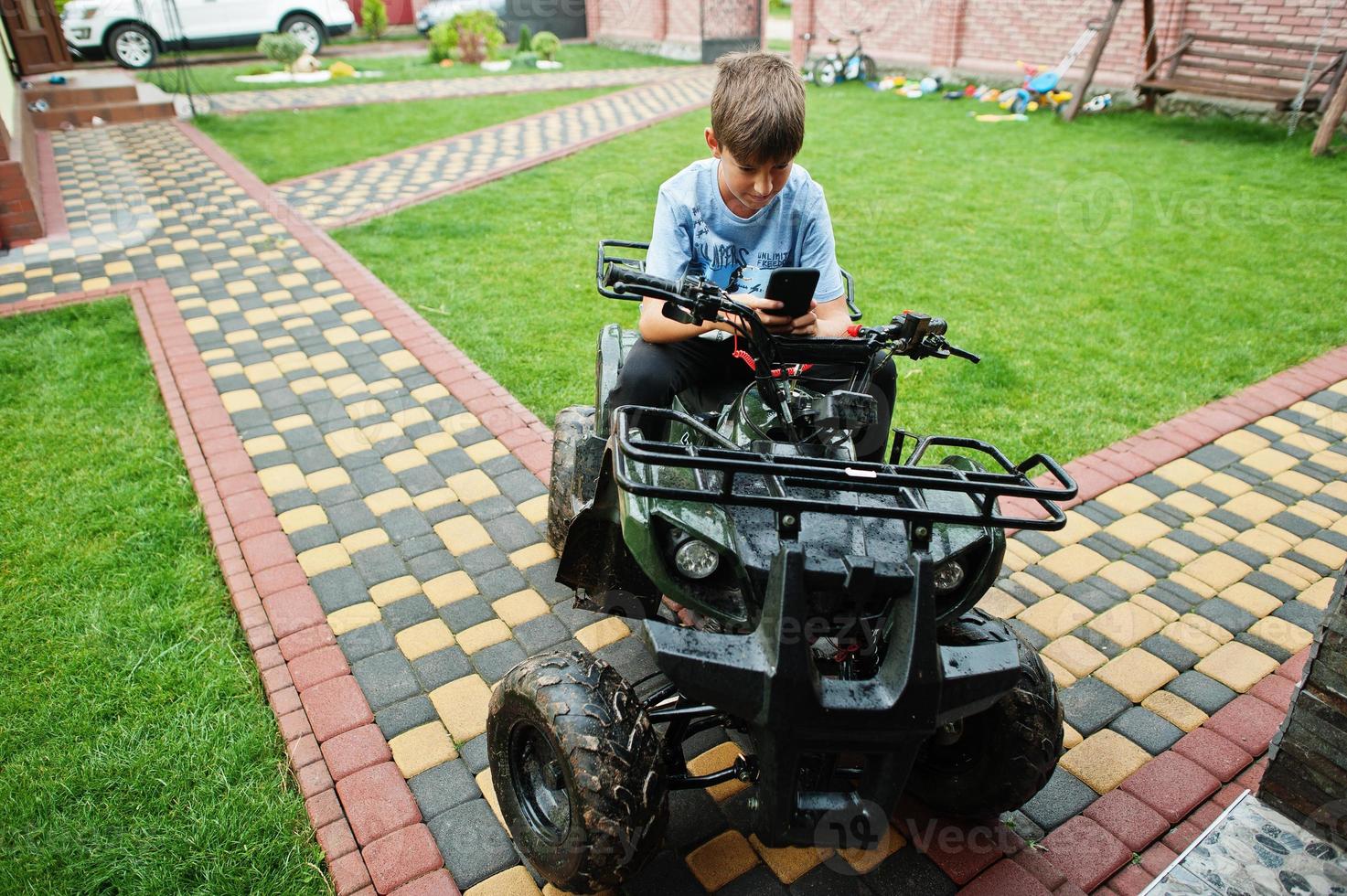 menino em quadriciclo de quatro rodas com telefone celular. foto
