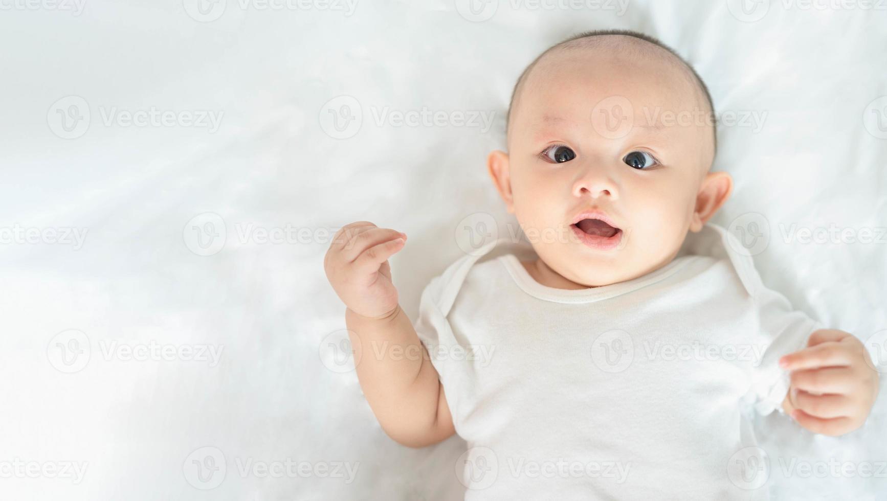 família feliz, bonito bebê recém-nascido asiático deitado jogar na cama branca olhe para a câmera com sorriso sorridente rosto feliz. pequena inocente criança adorável infantil no primeiro dia de vida. conceito de dia das mães. foto