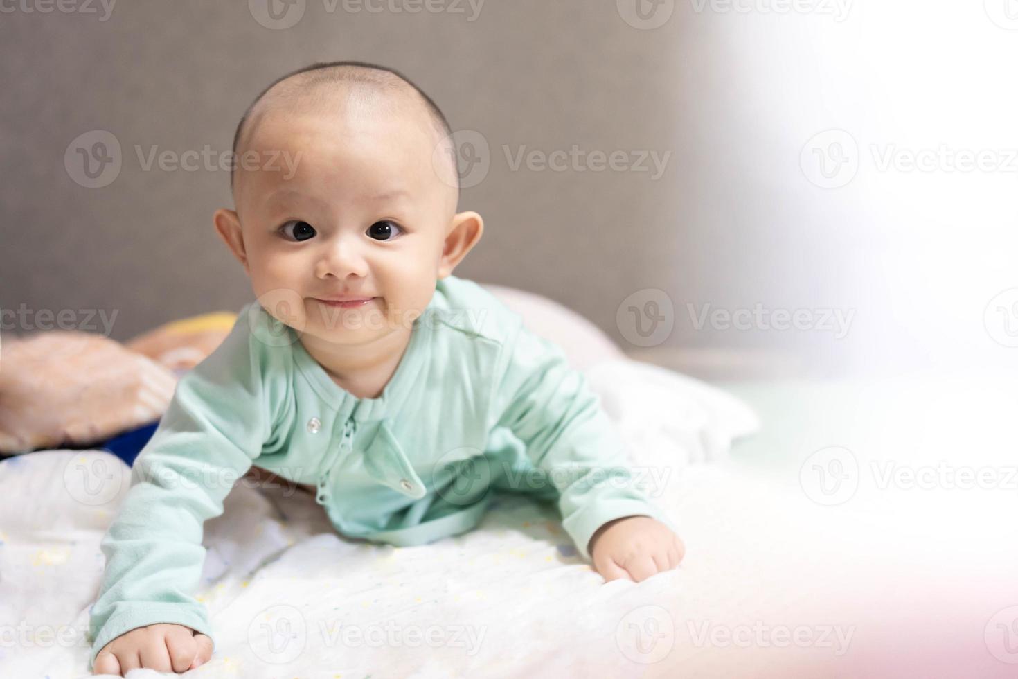 família feliz, bebê recém-nascido asiático fofo usa camisa azul deitado, rastejando, brinca na cama branca com sorriso sorridente rosto feliz. criança adorável infantil inocente no primeiro dia de vida. conceito de dia das mães. foto