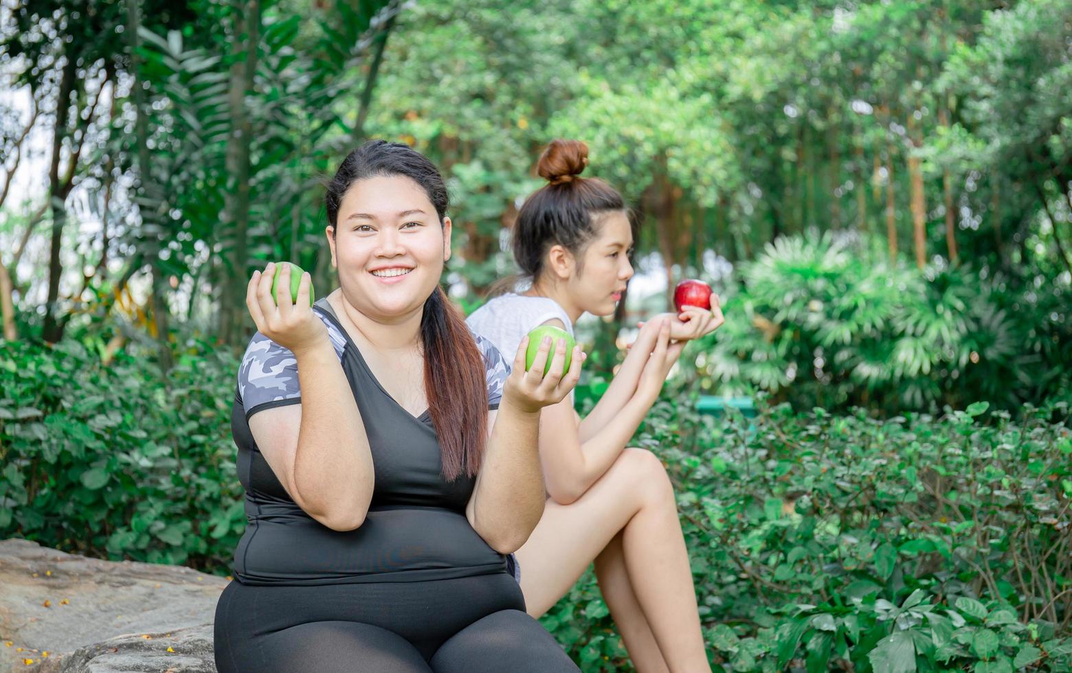 mulheres jovens sorridentes segurando uma maçã sentada relaxam no parque, conceito saudável e estilo de vida foto