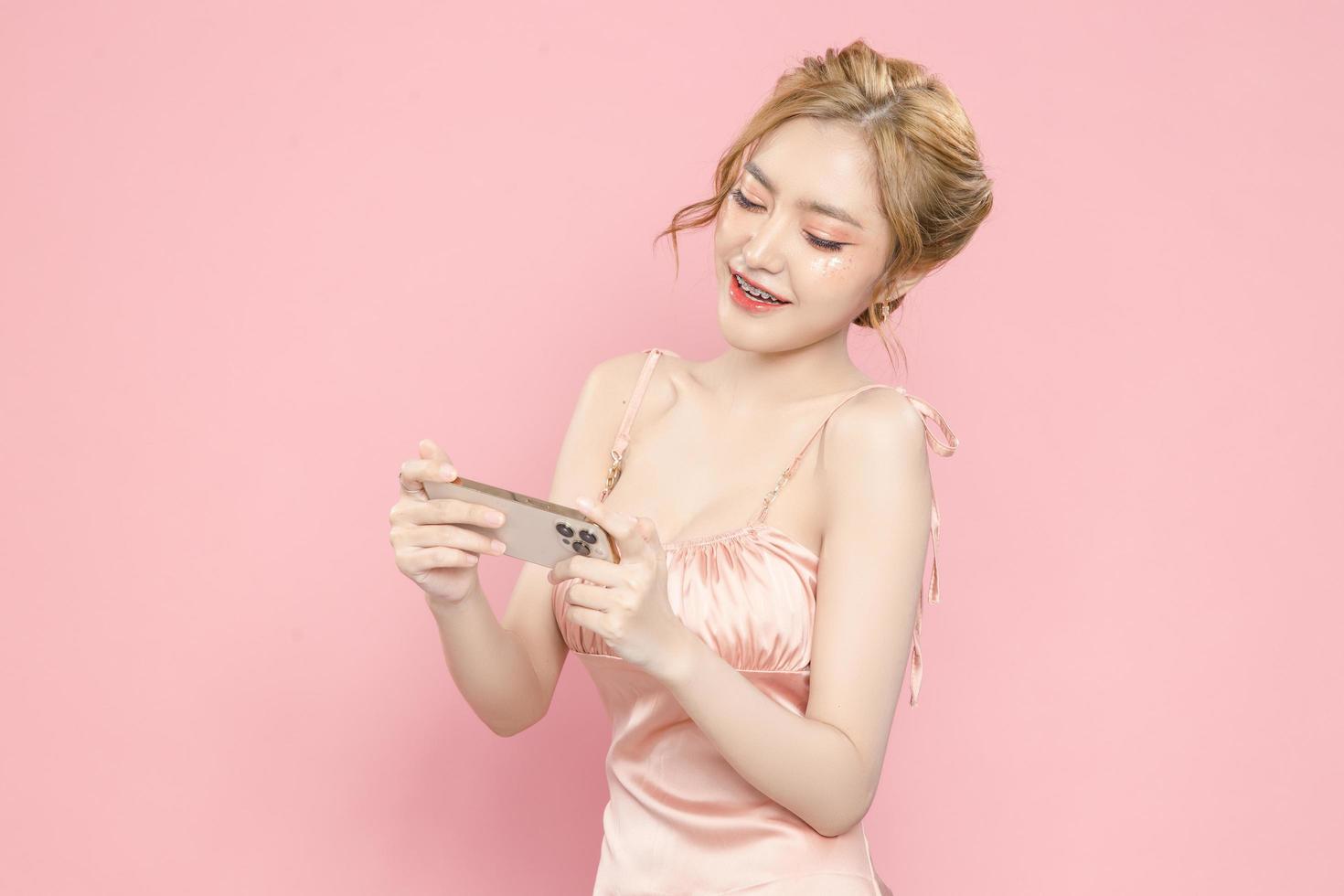 retrato alegre muito jovem asiática animada segurando o smartphone na mão no fundo rosa. grande oferta móvel, consumismo, conceito de estilo de vida. foto