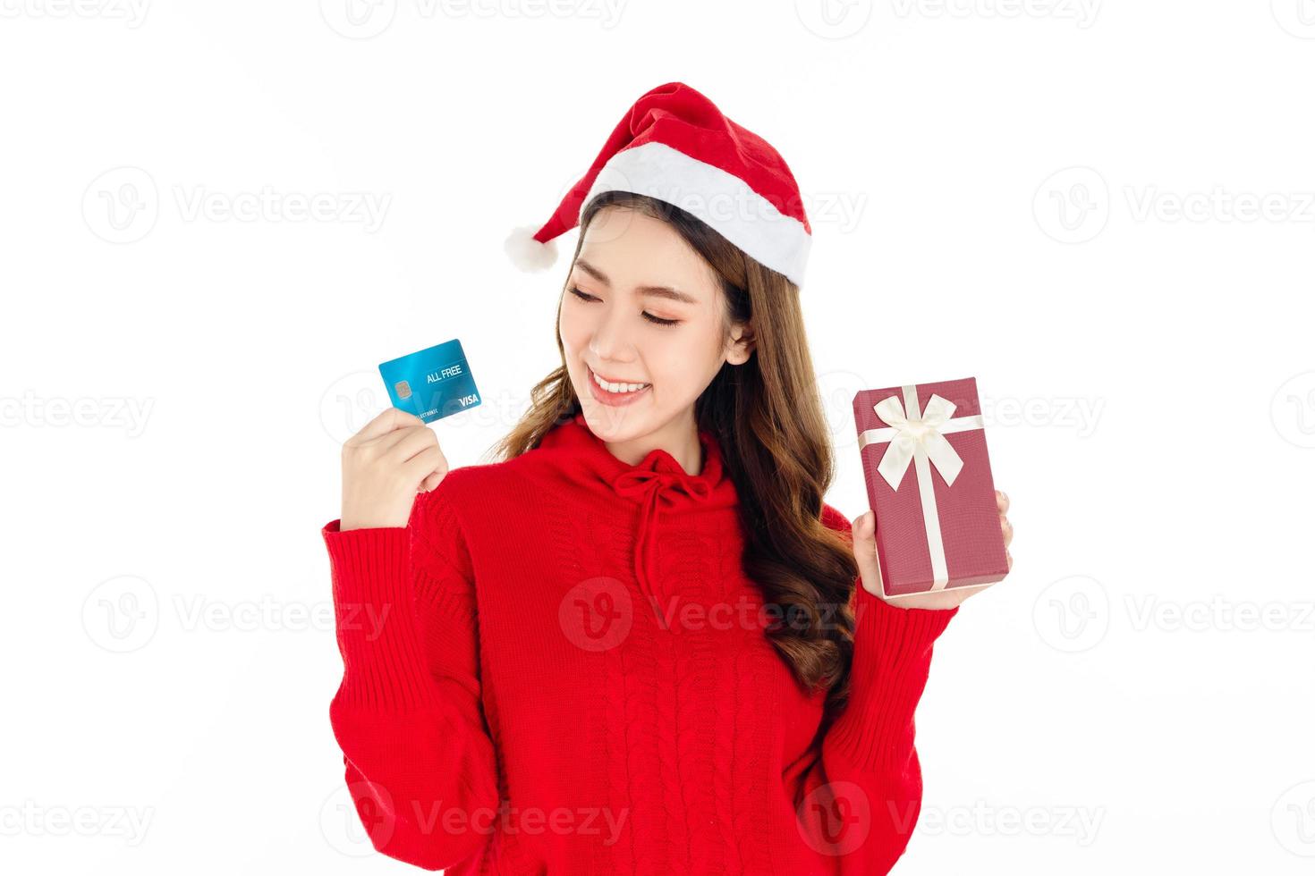 uma linda mulher asiática usando um vestido vermelho com um chapéu de papai noel está segurando uma caixa de presente. conceito de compras. foto
