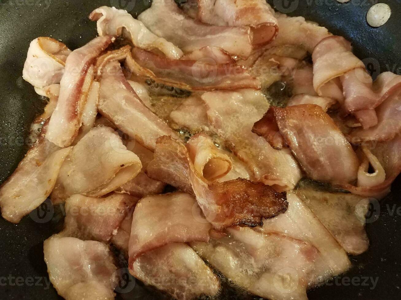 bacon cozinhando na frigideira ou frigideira no fogão foto