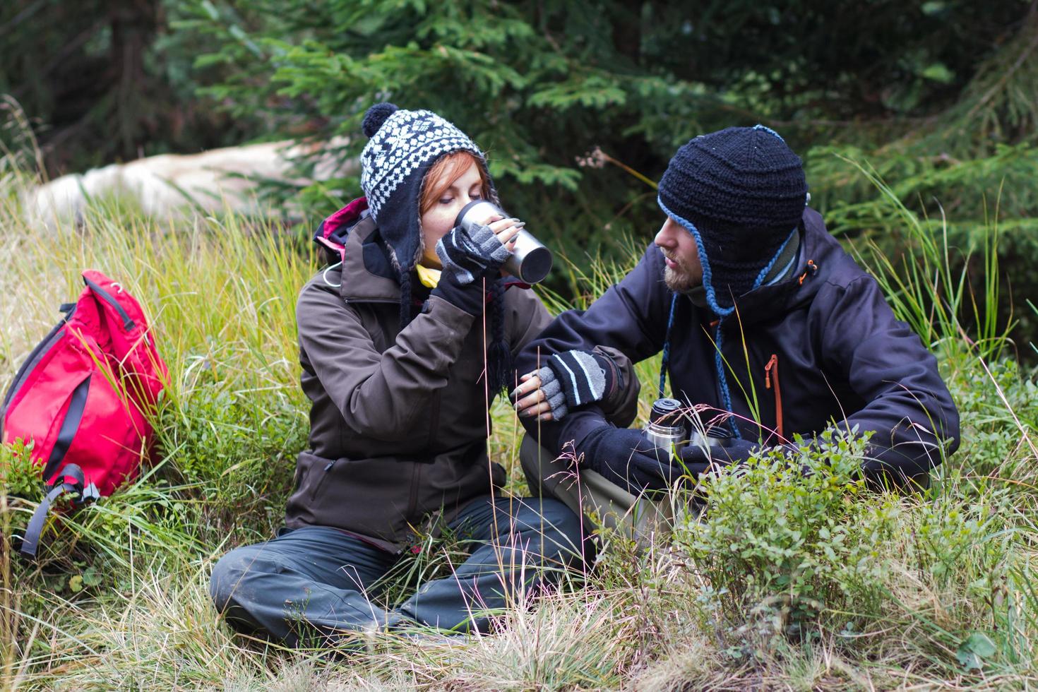 jovem casal caminhante com copos térmicos na floresta, viajantes em montanhas bebendo chá ou café foto