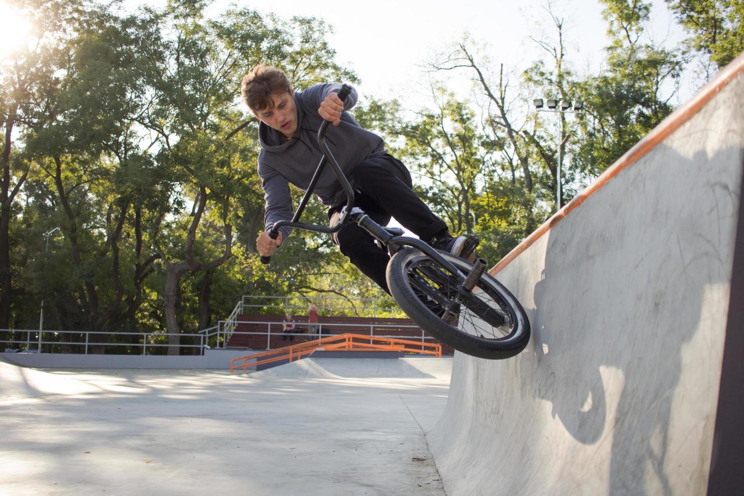 bmx rider treinando e fazendo truques na street plaza, bicyxle stunt rider em coccrete skatepark foto