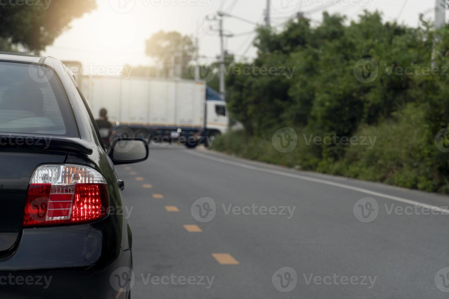 parte traseira do carro preto acende a luz de freio para parar na estrada de asfalto. caminhões de contêineres estacionados bloqueando o tráfego. estradas em áreas provinciais com árvores ao lado da estrada. foto