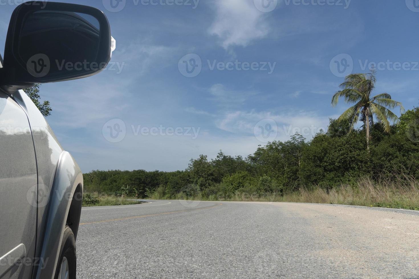 vista lateral de um carro cinza coberto de areia executado na estrada de asfalto. estrada é sinuosa e há areia ao lado da estrada. grama verde na beira da estrada sob o céu azul. foto