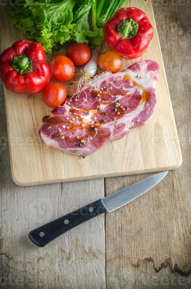carne de porco crua na tábua e legumes facas. foto