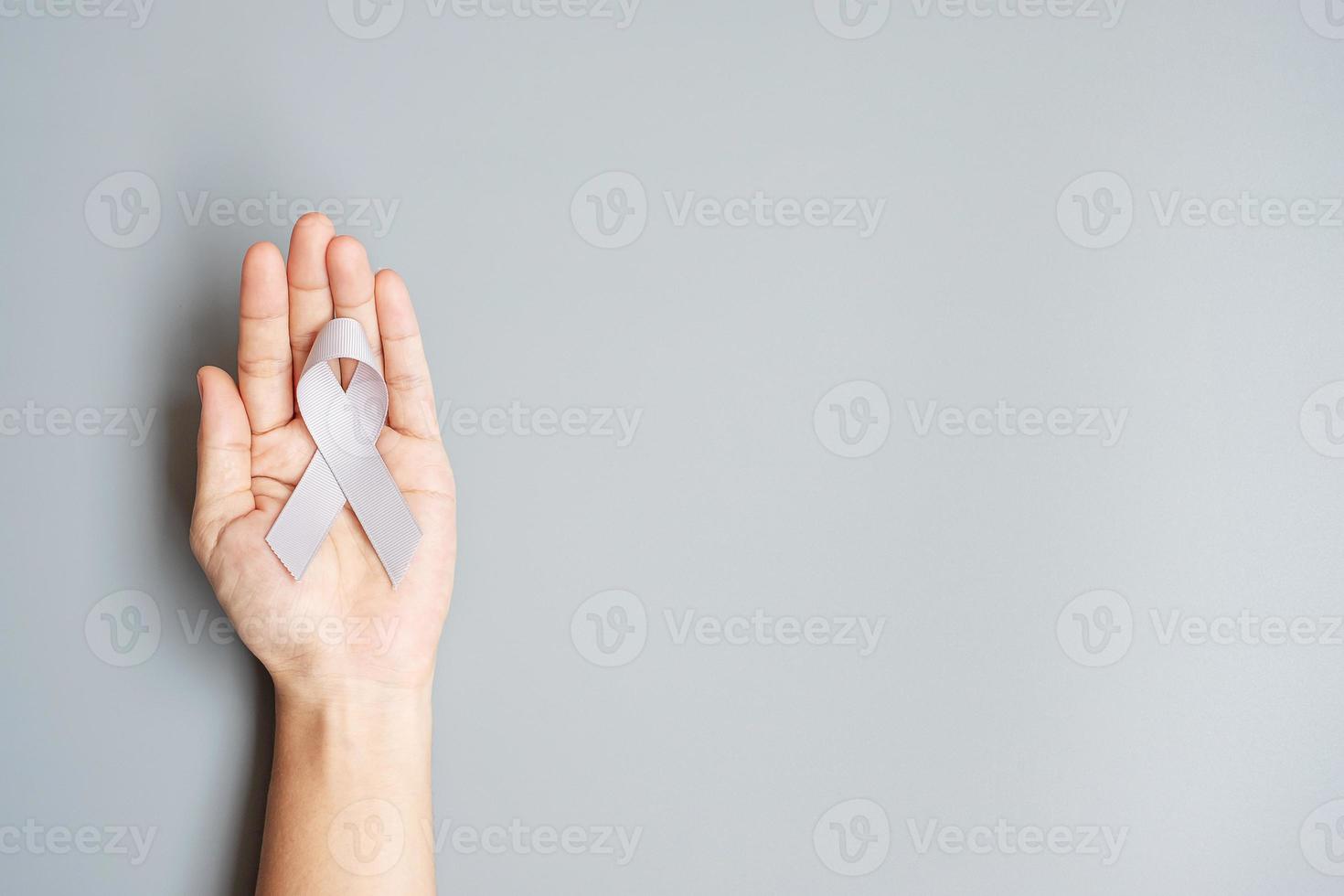 mês de conscientização do câncer cerebral, mão de mulher segurando a fita de cor cinza para apoiar as pessoas que vivem. conceito de saúde e dia mundial do câncer foto