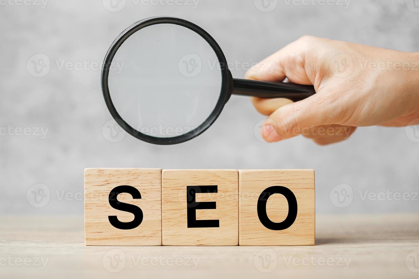 seo search engine optimization texto blocos de cubo de madeira e mão segurando a lupa na mesa. ideia, estratégia, publicidade, marketing, palavra-chave e conceito de conteúdo foto