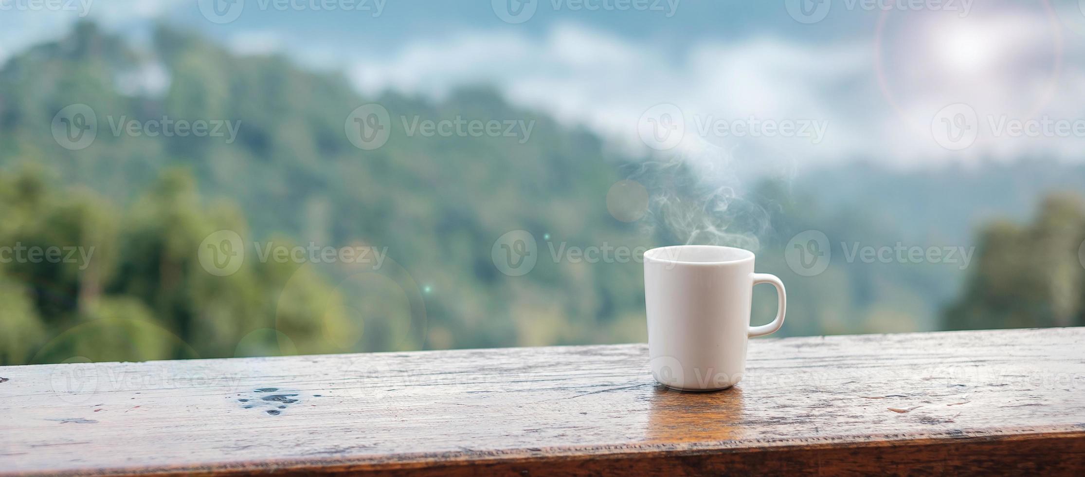 caneca branca de café quente ou chá na mesa de madeira pela manhã com fundo de montanha e natureza foto