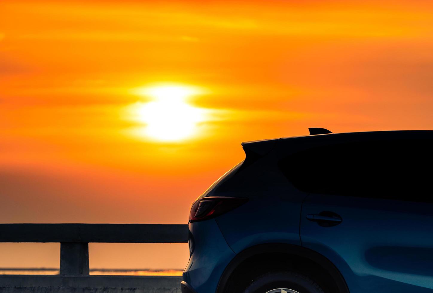 carro suv compacto azul com esporte e design moderno estacionado na estrada de concreto à beira-mar ao pôr do sol à noite. conceito de tecnologia de carro híbrido e elétrico. vaga de estacionamento. indústria automobilística. foto