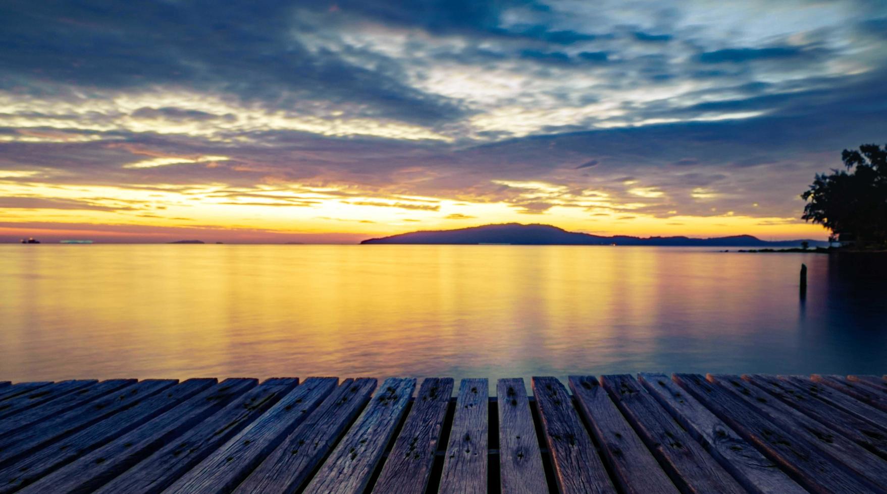 cais de madeira com mar e montanha ao nascer do sol com lindo céu dourado de manhã e espaço de cópia usado como pano de fundo para exibir mercadorias e produtos. foto