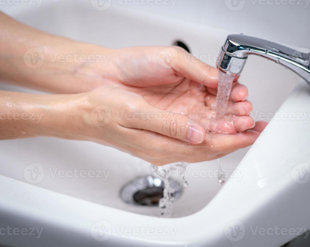 mulher lavando a mão com água da torneira no banheiro. mão limpa sob torneira na pia para higiene pessoal. primeiro passo para limpar as mãos sujas para prevenir gripe e coronavírus. bom procedimento de lavagem das mãos. foto