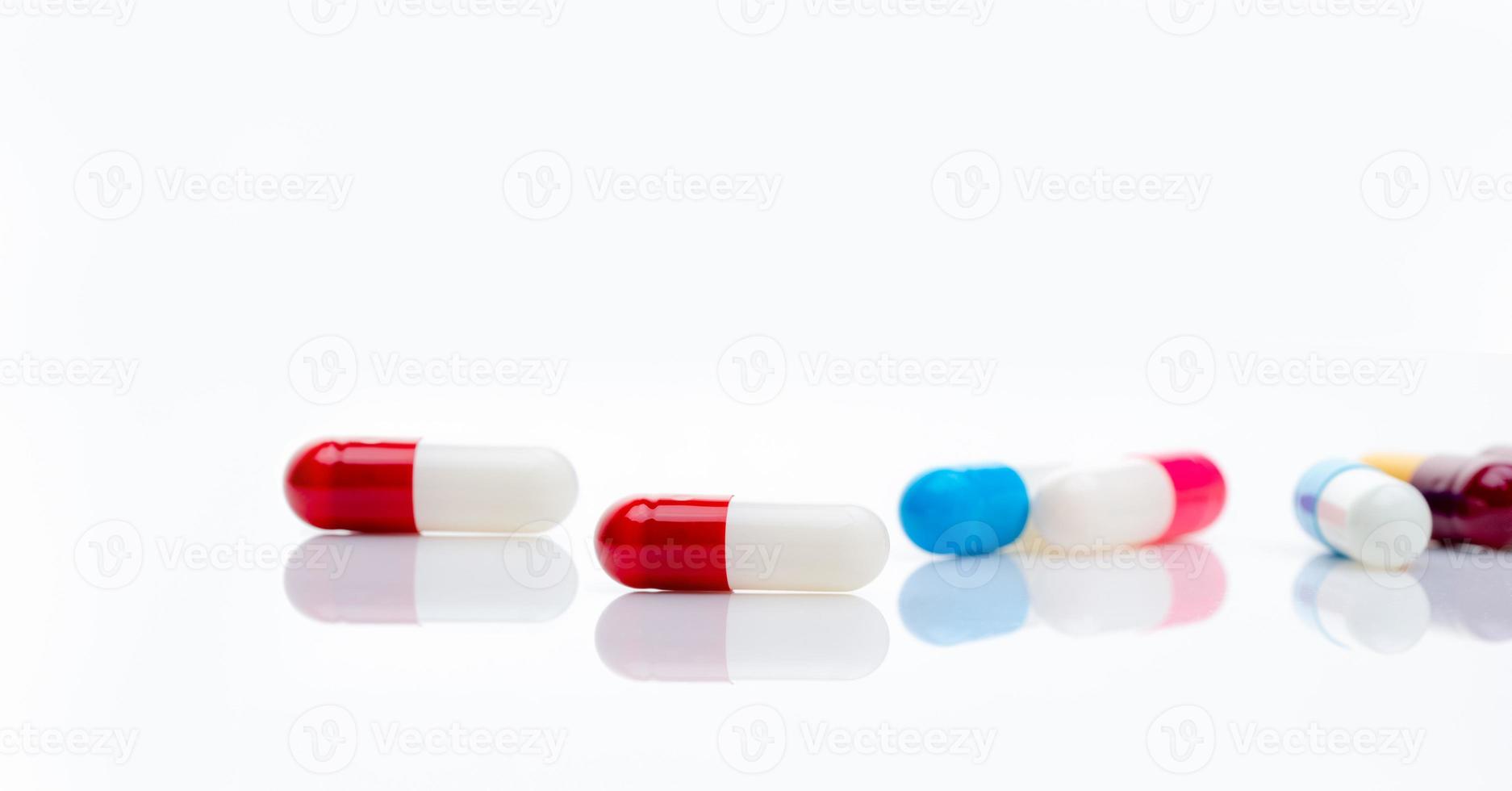 pílula de cápsula de antibiótico vermelho-branco no fundo de cápsulas multicoloridas desfocadas. conceito de resistência a antibióticos. banner horizontal de farmácia. medicamentos prescritos. indústria farmacêutica. cuidados de saúde. foto