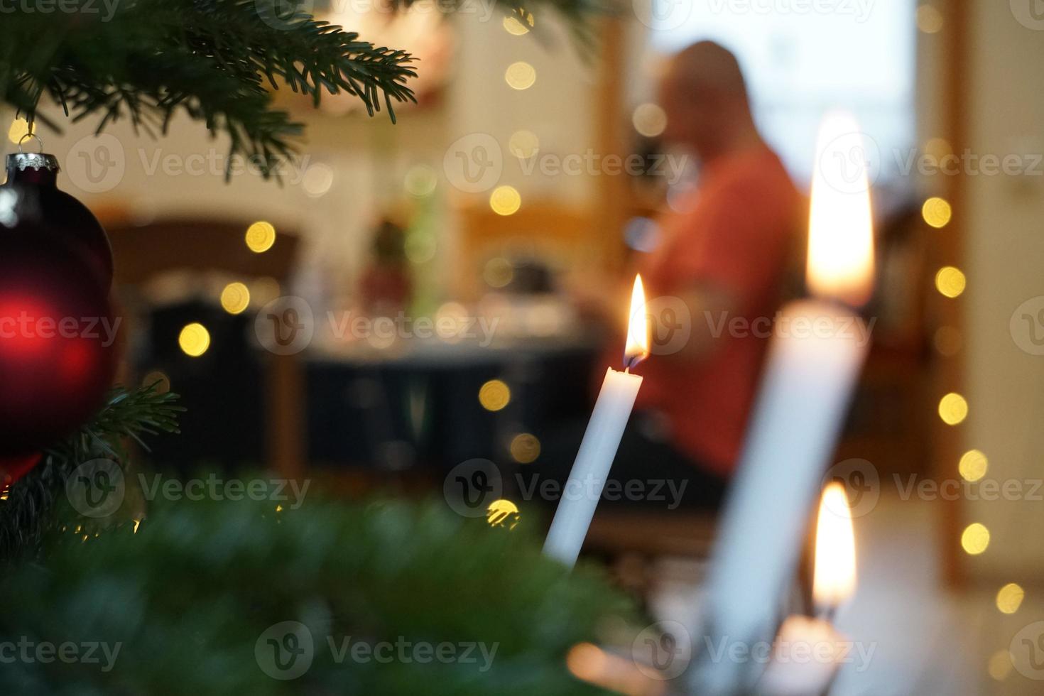 luz de velas de cera na árvore de natal verde. e silhueta de pessoas foto