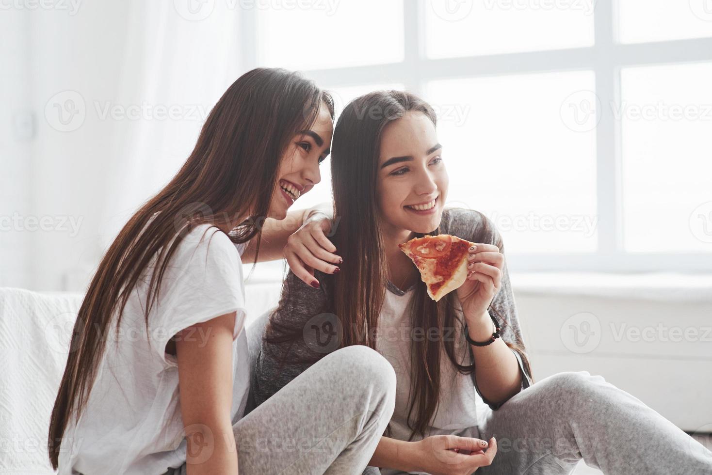 engraçado filme de comédia. irmãs comendo pizza ao assistir tv enquanto se senta no chão do lindo quarto durante o dia foto