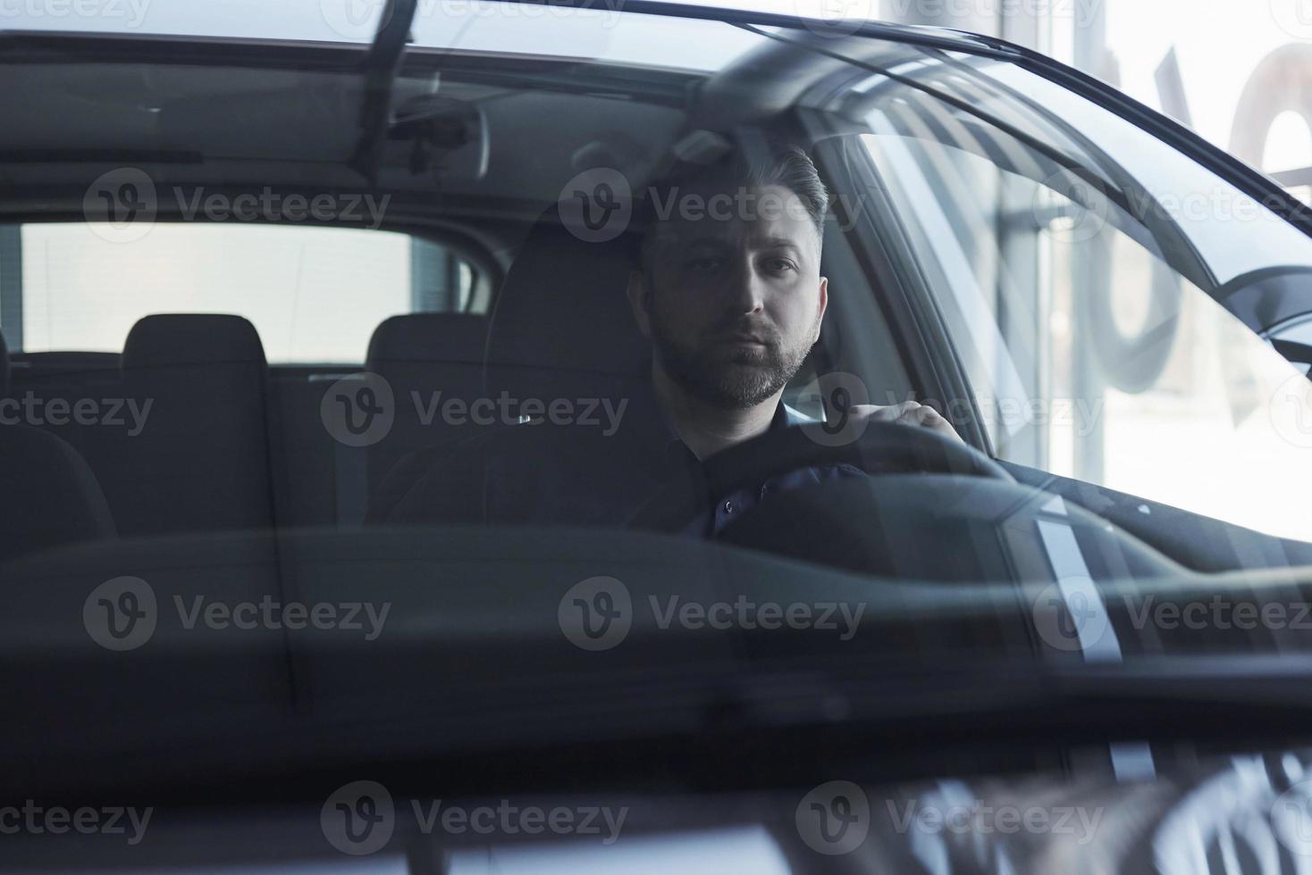 indo para o trabalho. vista frontal do jovem empresário barbudo sentado em seu carro preto de luxo foto