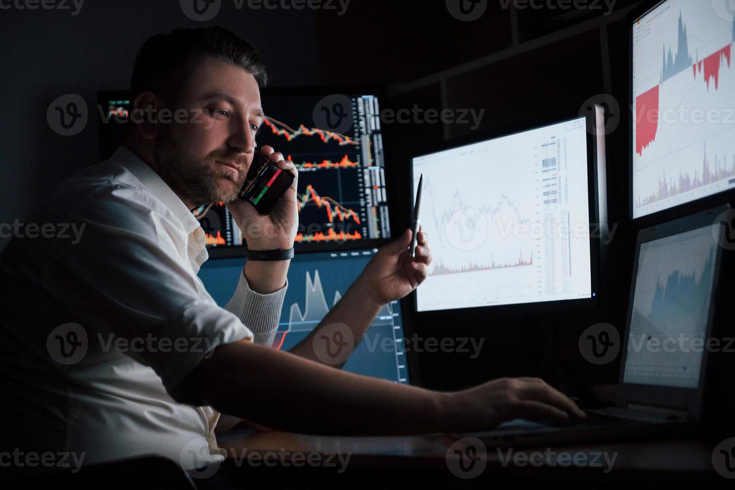 cara ocupado. homem barbudo de camisa branca trabalha no escritório com várias telas de computador em gráficos de índice foto