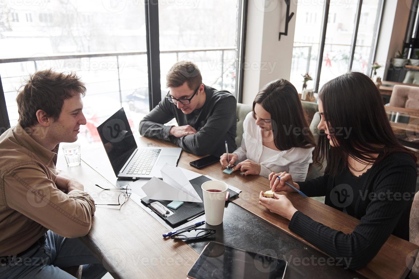 fazendo um plano. quatro jovens estudantes trabalhando no projeto sentados na sala perto da janela foto