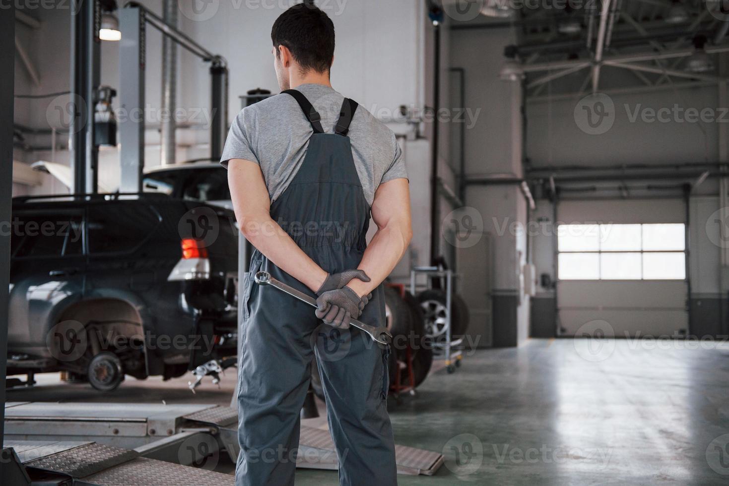 olhando para os carros. vista traseira do trabalhador de uniforme que fica na oficina com chave na mão foto