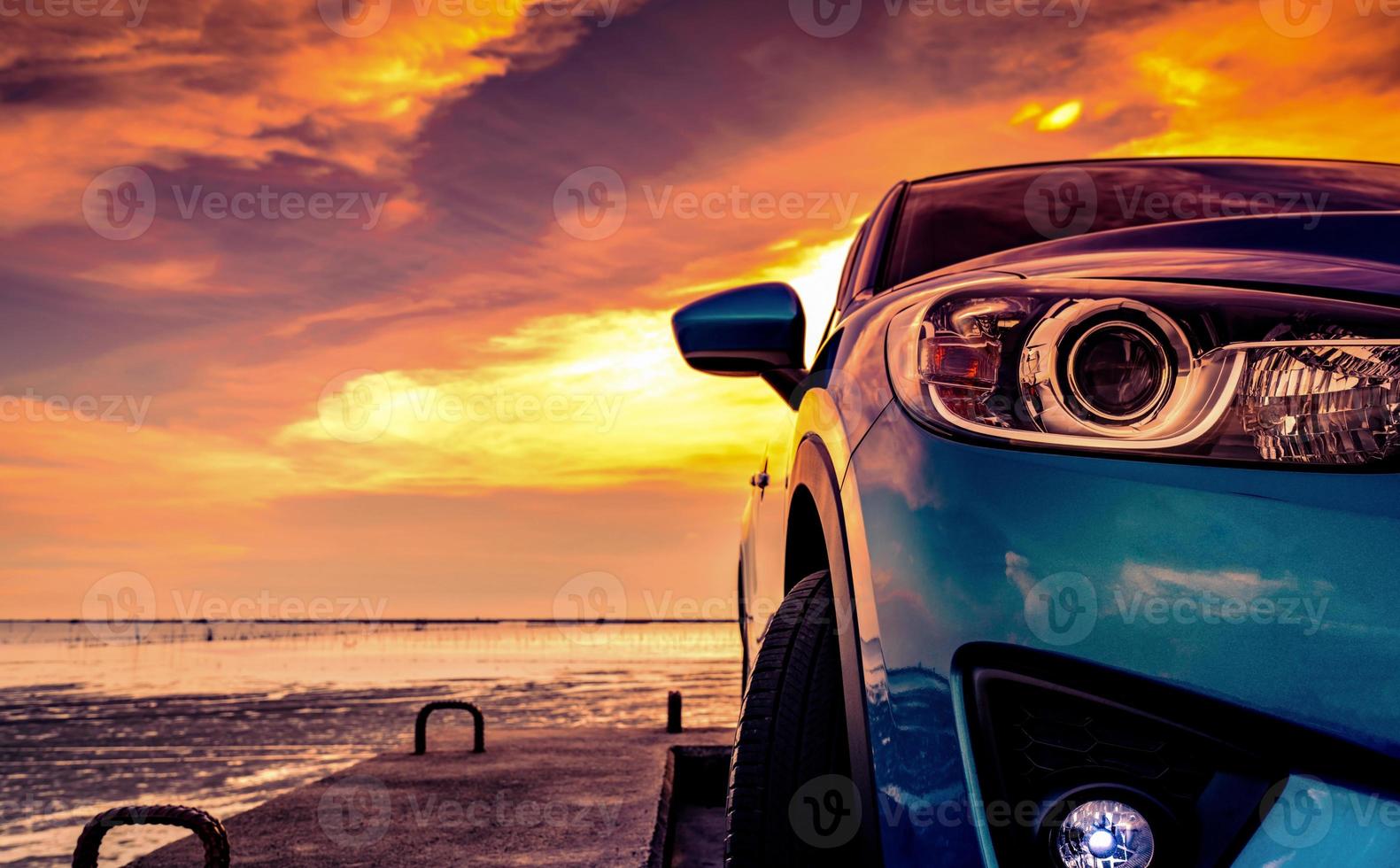 carro suv compacto azul com design esportivo e moderno estacionado na estrada de concreto na praia do mar ao pôr do sol. vista frontal do carro de luxo. lâmpada de nevoeiro suv closeup e faróis com lindo céu pôr do sol no verão. foto