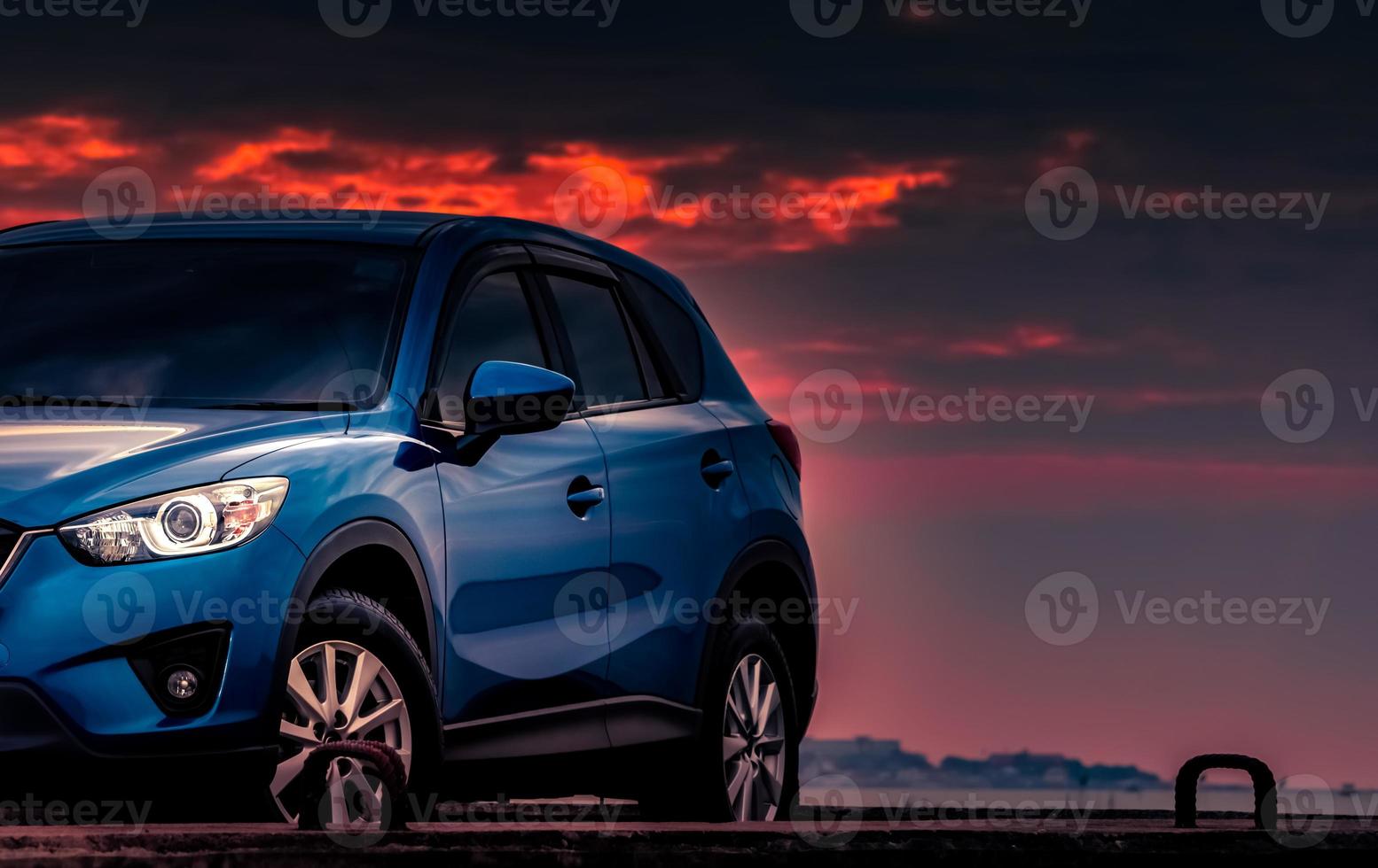 novo carro suv azul com design esportivo e de luxo estacionado na estrada de concreto à beira-mar ao pôr do sol com céu dramático e nuvens. indústria automobilística. tecnologia de carros híbridos e elétricos. viagens de verão à noite foto