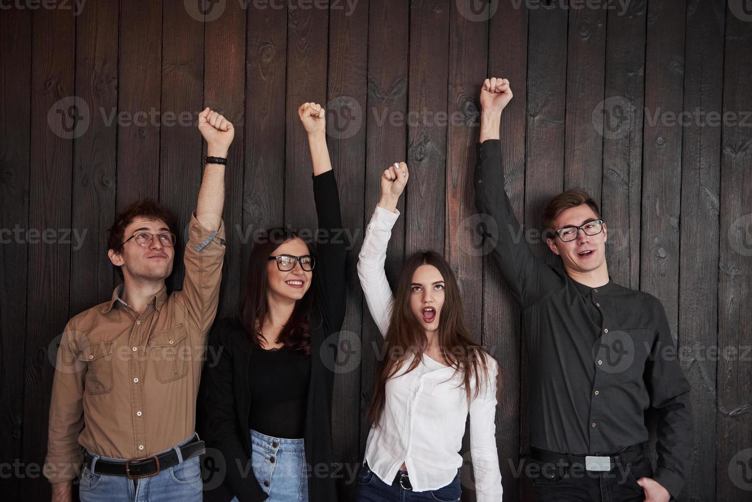 garota de camisa branca gritando. comemorando o sucesso. amigos colocam as mãos contra a parede de madeira preta foto