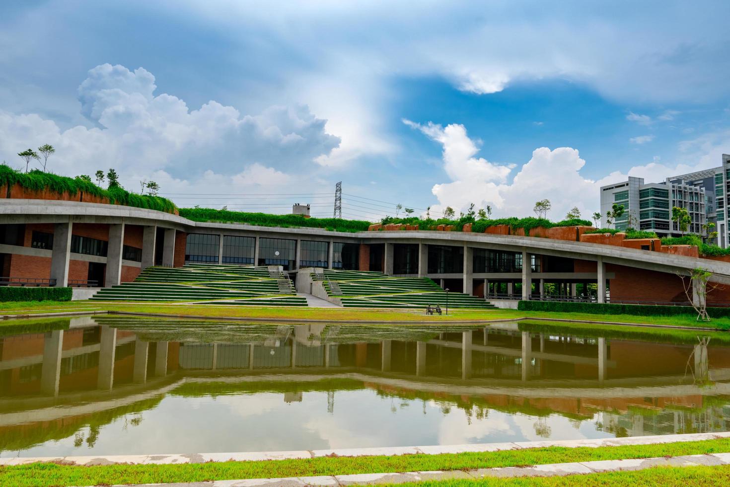 edifício de vidro ecológico com jardim vertical na cidade. árvore verde e hera na construção sustentável contra o céu azul e nuvens brancas. Arquitetura moderna. reflexo do edifício na água. foto