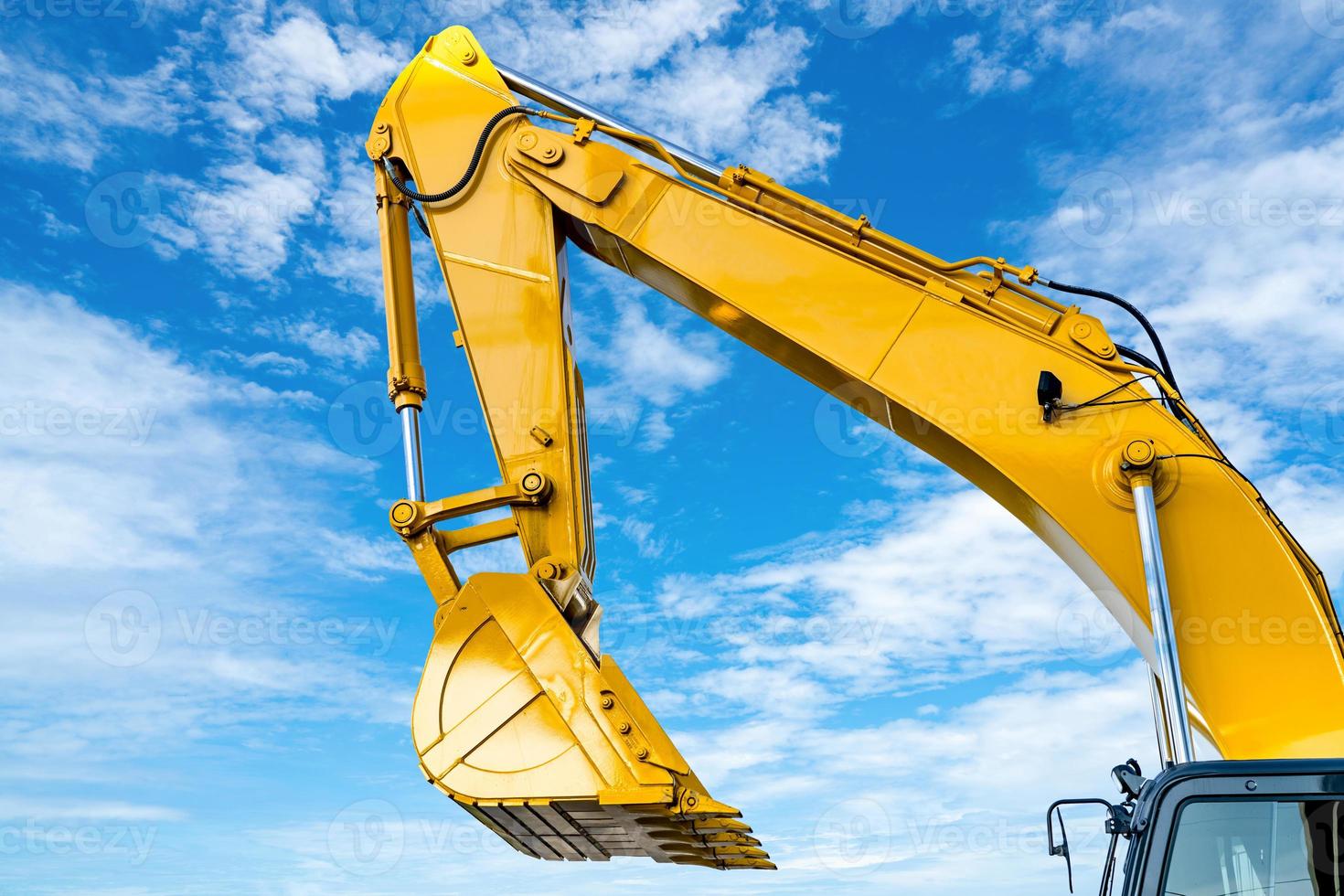 retroescavadeira amarela com braço de pistão hidráulico contra o céu azul. máquina pesada para escavação no canteiro de obras. máquinas hidráulicas. enorme escavadora. indústria de máquinas pesadas. Engenharia Mecânica. foto