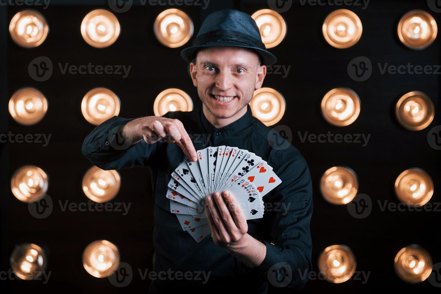 ele vai adivinhar o seu cartão. mágico de terno preto em pé na sala com iluminação especial nos bastidores foto