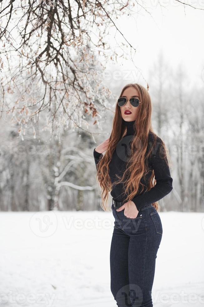 silêncio de inverno. menina bonita com cabelo comprido na blusa preta e óculos está na floresta de neve foto