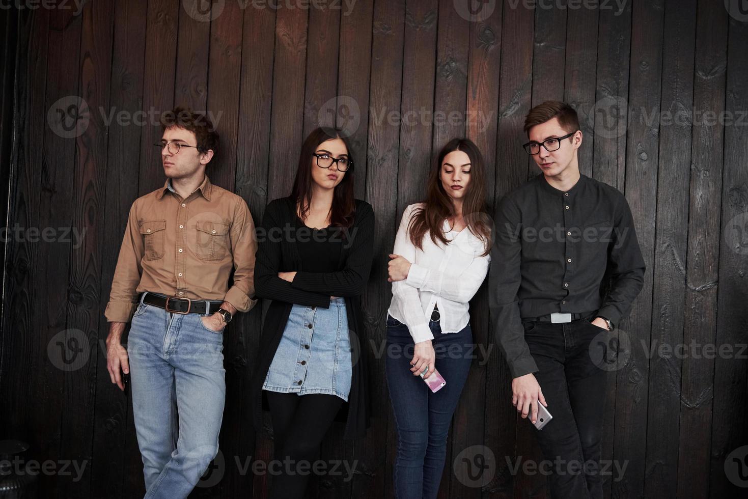 esperando tanto tempo. juventude fica contra a parede de madeira preta. grupo de amigos passando tempo juntos foto