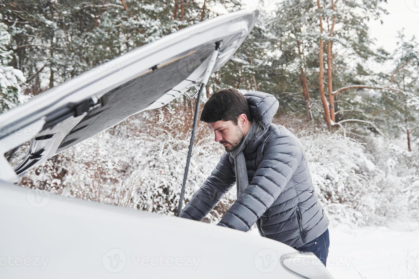 cara preso na floresta de inverno porque seu carro tem alguns problemas. tenta consertar automóvel foto