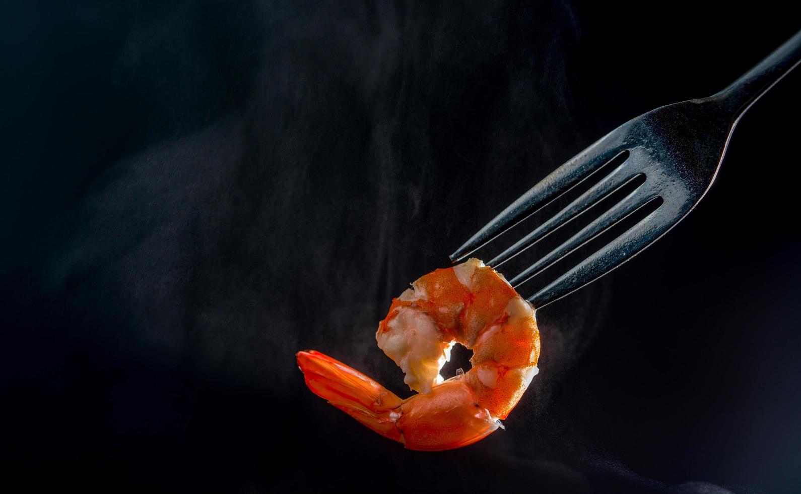 camarão cozido no vapor no garfo isolado em fundo escuro com espaço de cópia. buffet de frutos do mar no conceito de restaurante. use para publicidade de promoções de buffet de frutos do mar foto