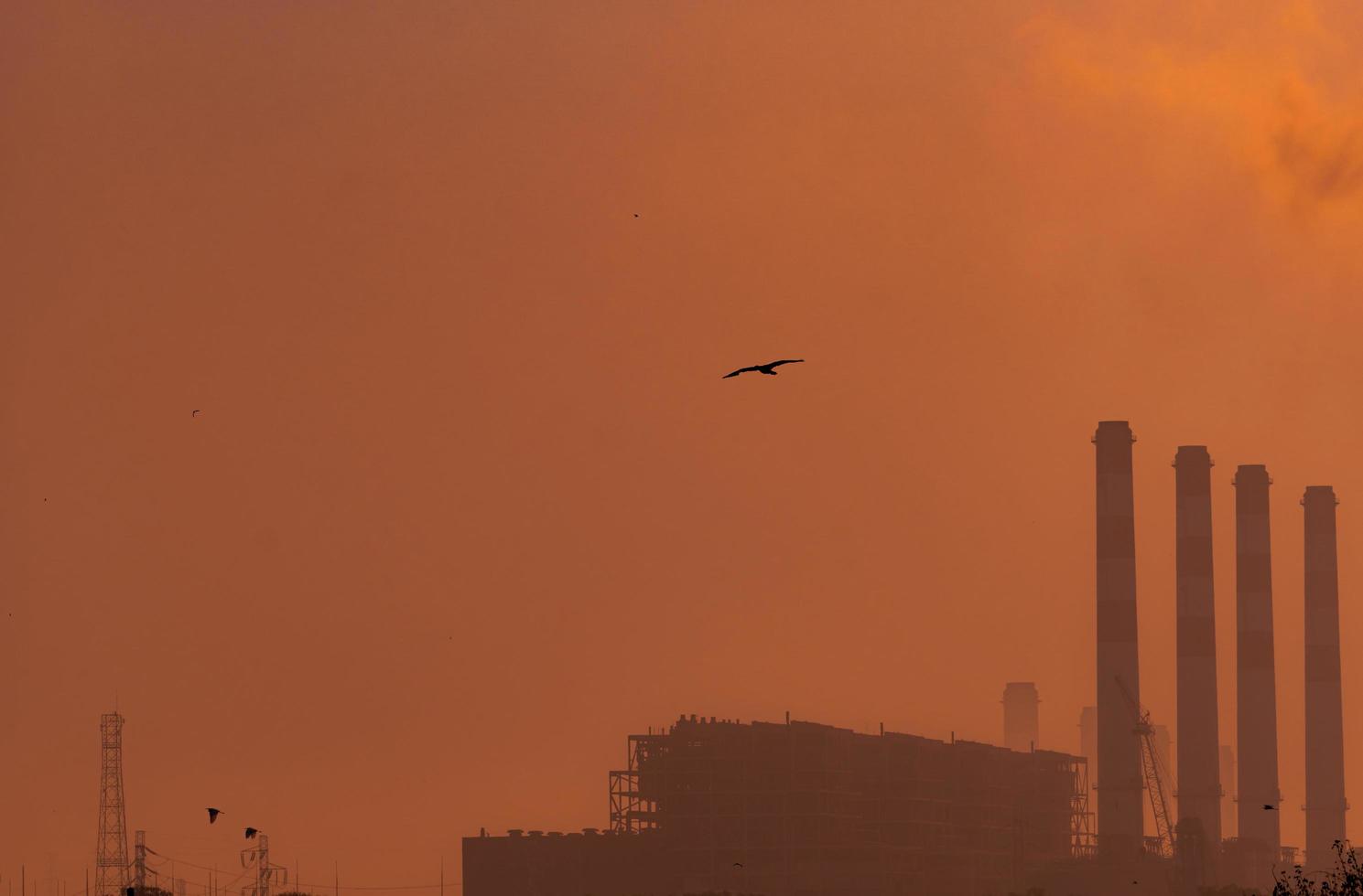 usina com céu laranja do sol e pássaros voando no céu. conceito de poluição do ar. energia para fábrica de apoio em parque industrial. potência e energia. poeira se espalhou no ar à noite. foto