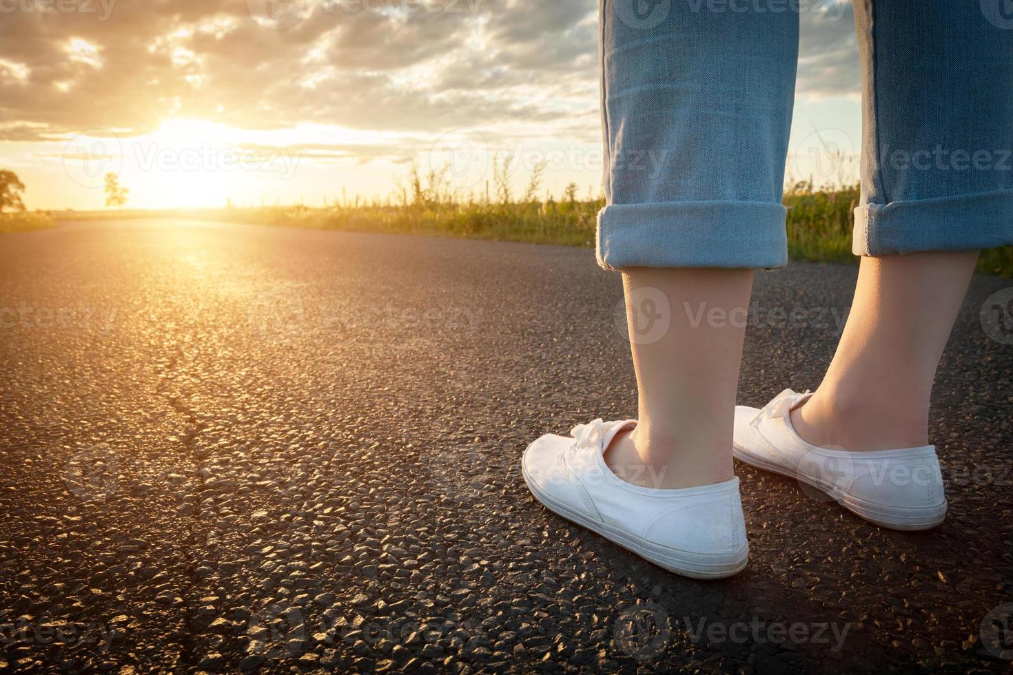 mulher de tênis branco em pé na estrada de asfalto em direção ao sol. viagens, conceitos de liberdade. foto