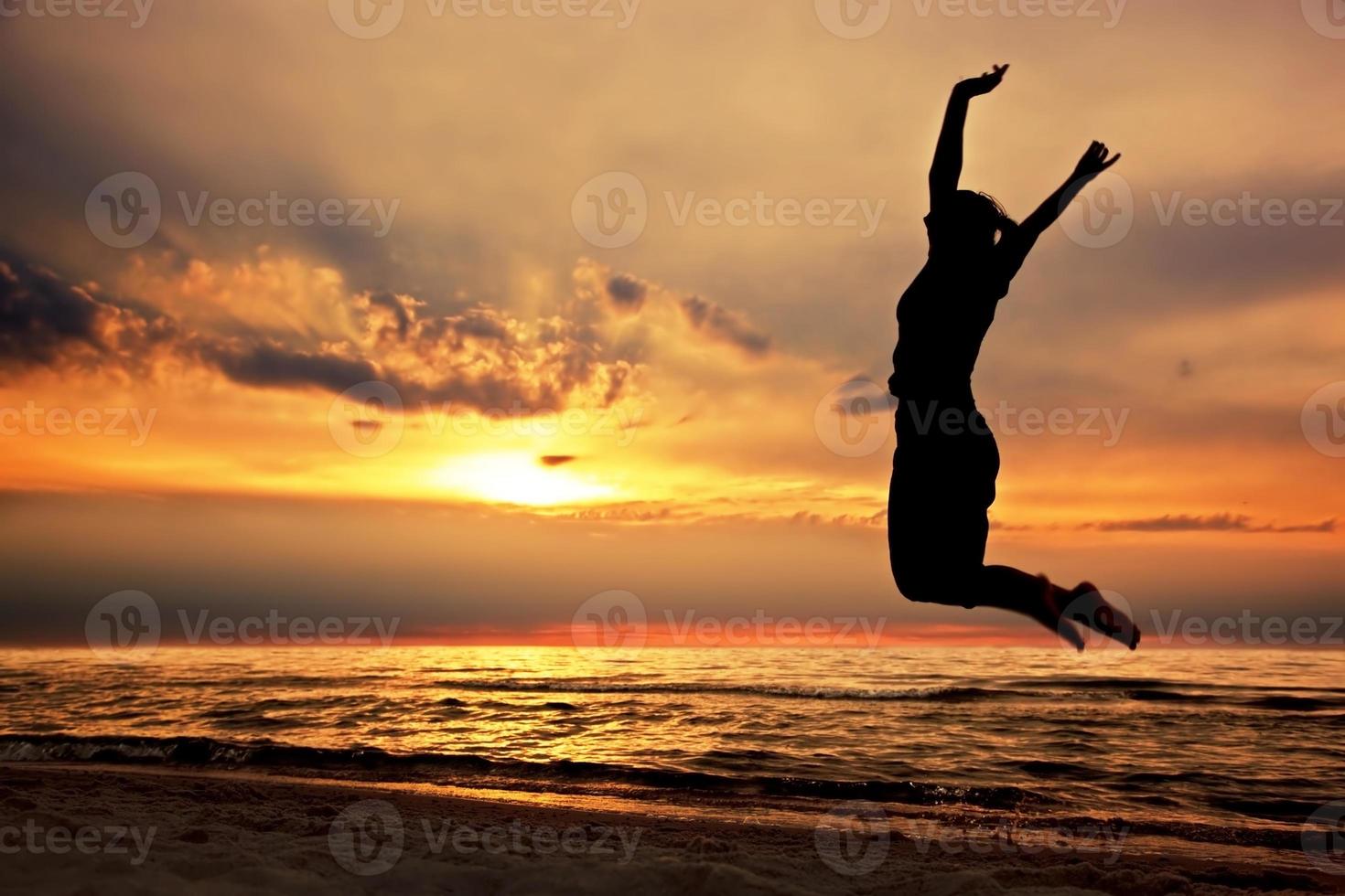 mulher feliz pulando na praia ao pôr do sol foto