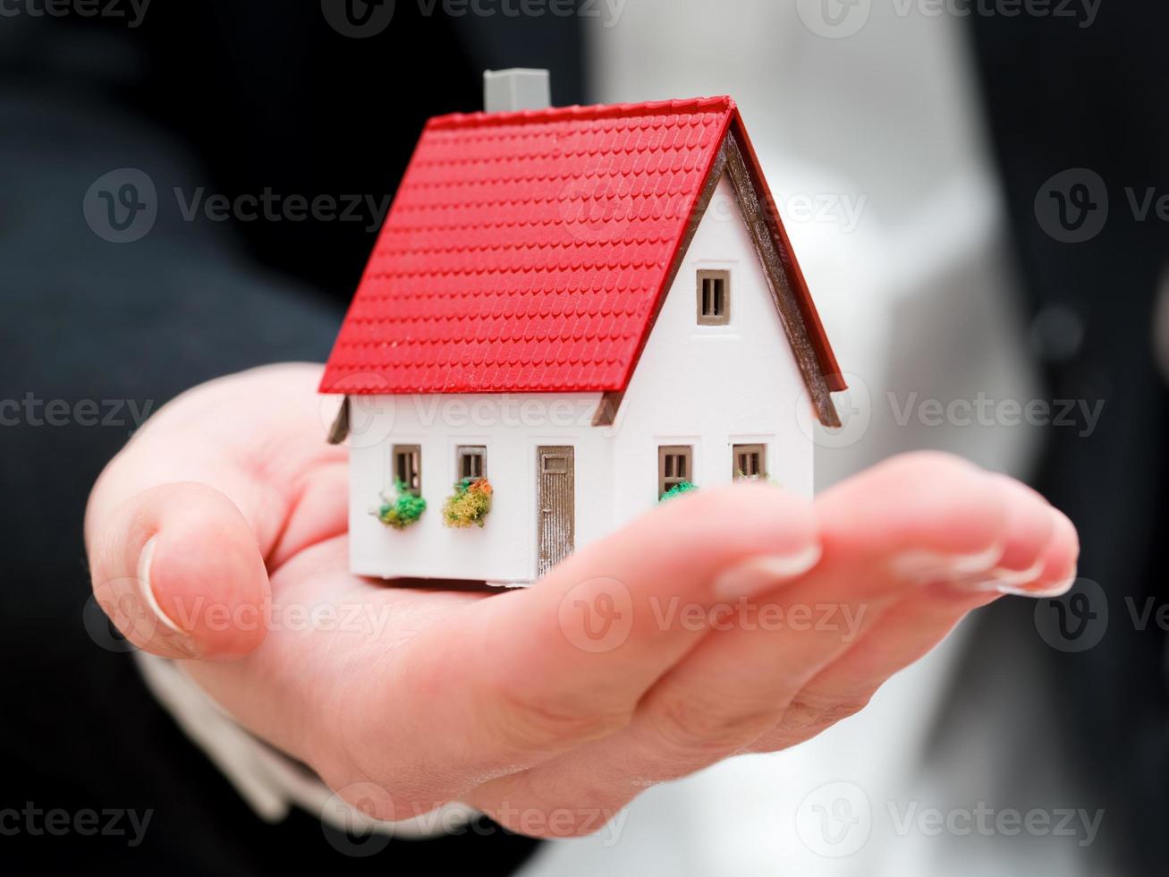 um agente imobiliário segurando uma pequena casa nova em suas mãos foto
