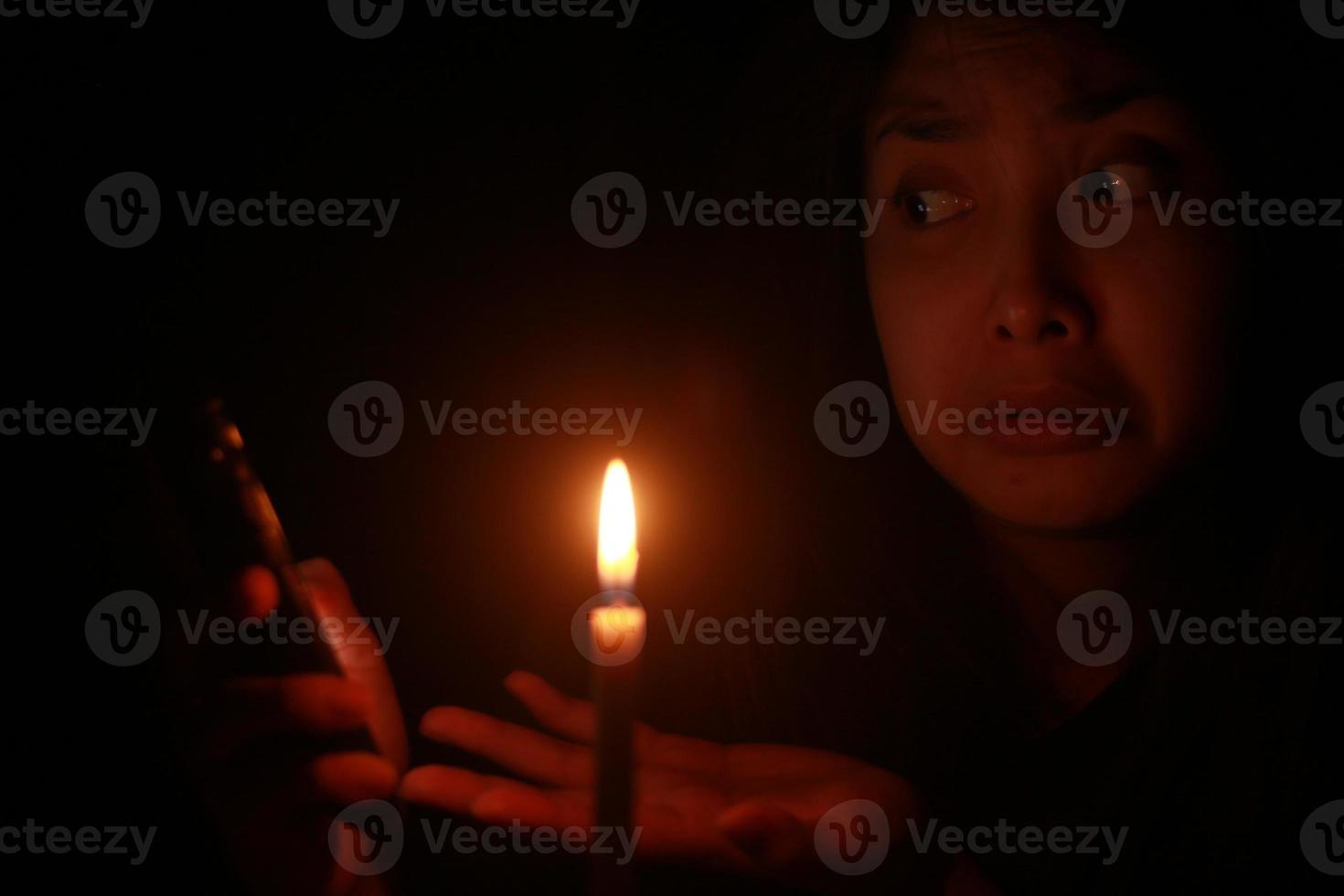 uma mulher asiática chocante apontando o celular na frente da luz de velas na noite escura foto