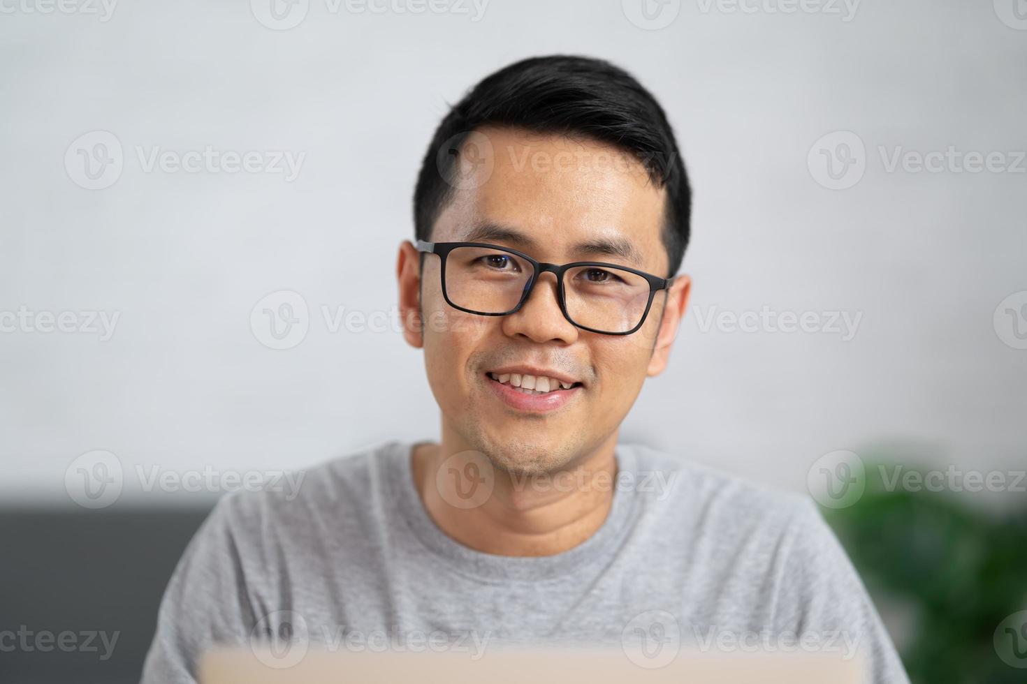 homem freelance em óculos sorrindo e trabalhando com laptop remotamente, sentado à mesa de madeira. homem feliz agradável se comunicando na rede social, pesquisando informações online. foto